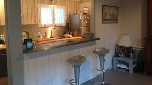 Una cocina con armarios de madera, un refrigerador, un lavamanos y dos taburetes de bar.