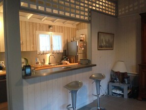 Uma cozinha com armários de madeira, geladeira, pia e dois bancos.