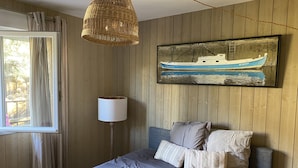 Un dormitorio con cama, lámpara colgante, un cuadro de un barco y paneles de madera en las paredes.