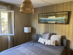 Quarto com cama, luminária pendente, pintura de barco e painéis de madeira nas paredes.