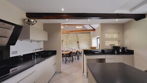 A modern kitchen with a built-in oven, a dining area with a stone wall, and a coffee station. - Les lodges de la Baie Servon Mont Saint-Michel (Servon)