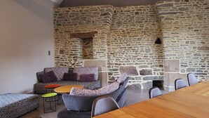 A cozy room with a stone wall, a sofa with patterned cushions, a wooden table, and a small coffee table. - Les lodges de la Baie Servon Mont Saint-Michel (Servon)