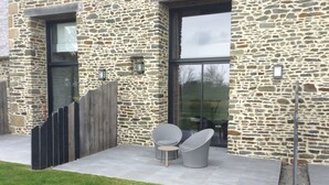 A stone building with a patio area featuring two chairs and a table. - Les lodges de la Baie Servon Mont Saint-Michel (Servon)