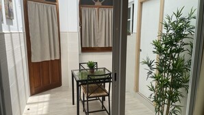 Passadís estret amb una porta de fusta, una taula de vidre i una cadira, i una planta en test.