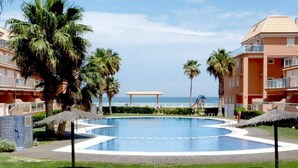 Une piscine bordée de palmiers, avec vue sur la plage et un espace abrité.