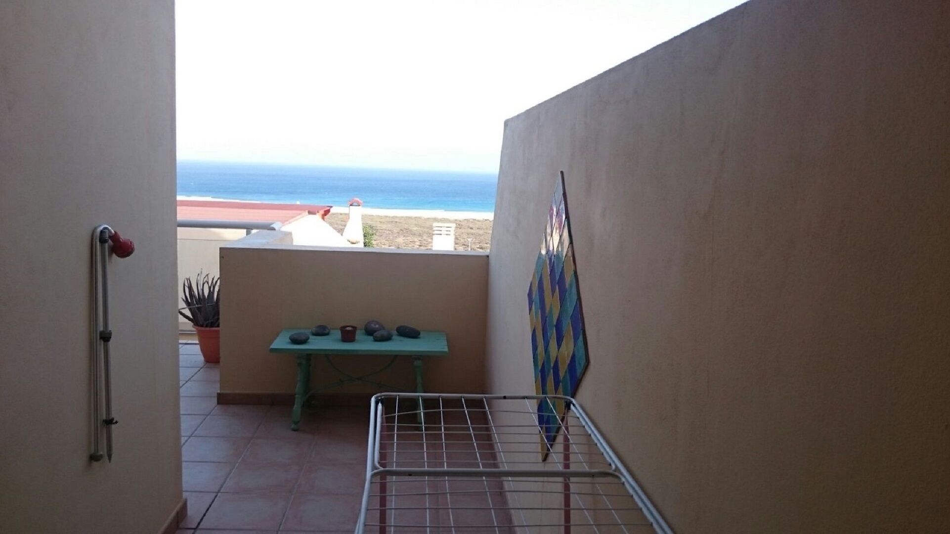 Een balkon met uitzicht op zee, een tafel met stenen en een metalen rek.