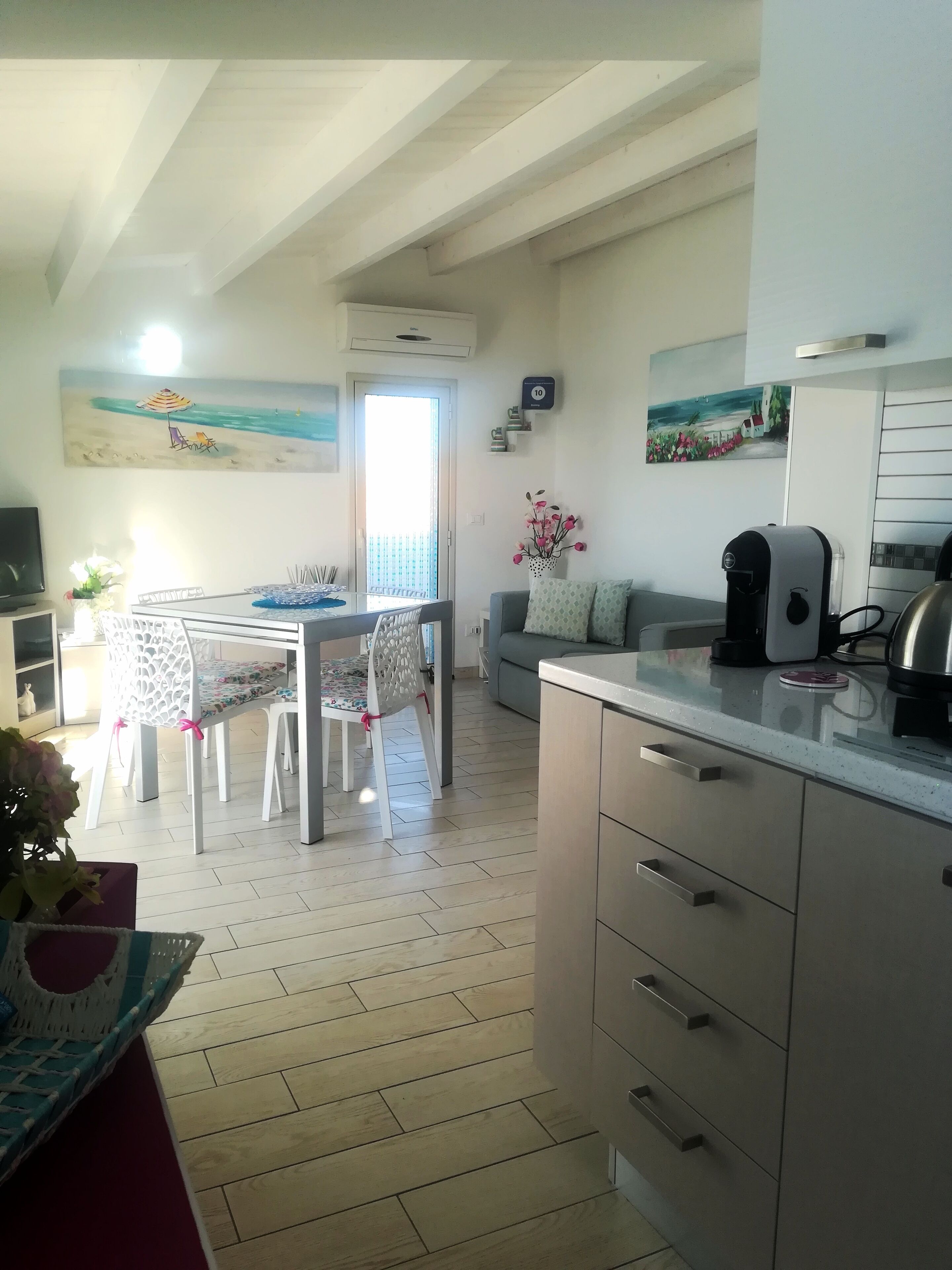 Eine moderne Küche mit Essbereich, mit Holzboden, Esstisch und Stühlen, einer Couch und einer Kaffeemaschine.