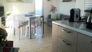 Una cocina moderna con comedor, que cuenta con suelo de madera, una mesa de comedor con sillas, un sofá y una cafetera.