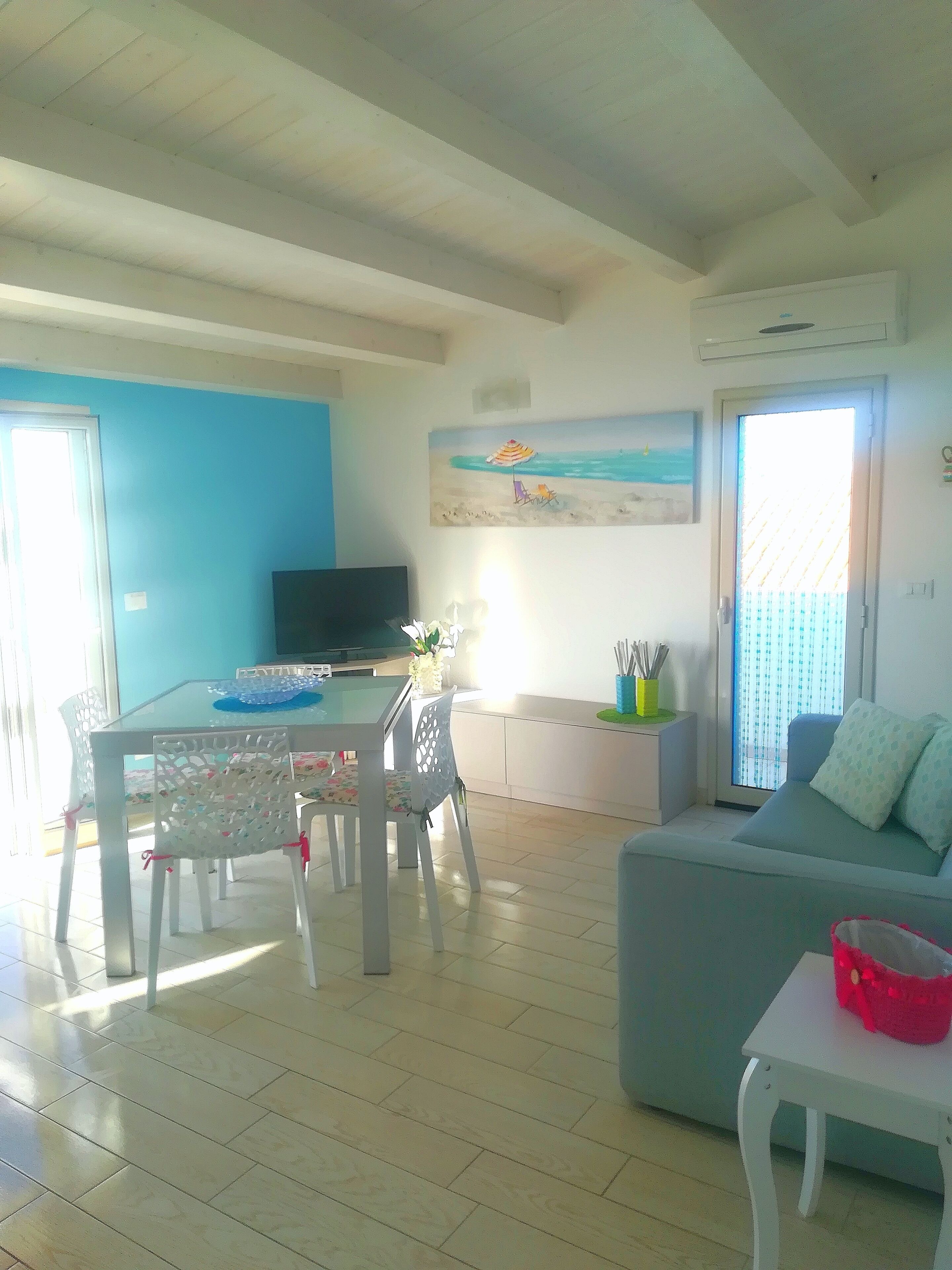 Un salon comprenant un canapé, une table à manger avec des chaises, un téléviseur et un tableau représentant une scène de plage.