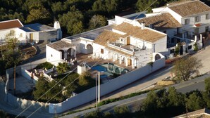 Eine weiße Villa mit Swimmingpool, umgeben von Grün und einer gepflasterten Straße.