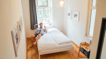 A single-bed room with a wooden floor, a bedside table with a glass, and a hanging light fixture.