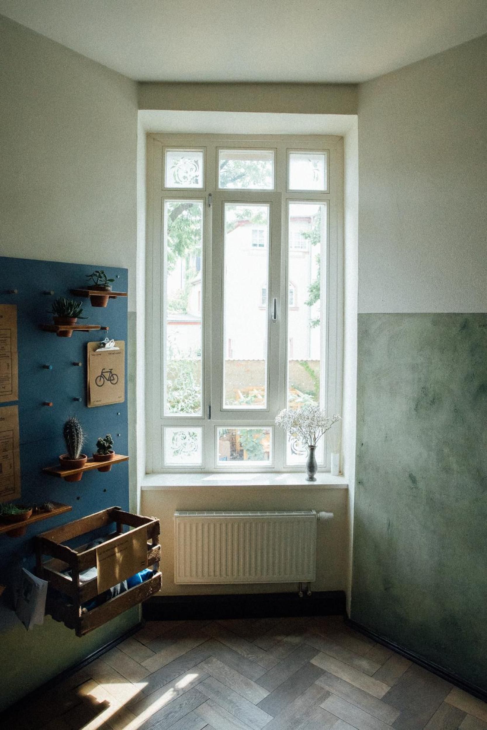 A room with a large window, wooden floor, and wall-mounted shelves with plants.