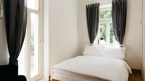 A bedroom with a bed, a window with curtains, and a view of greenery outside.