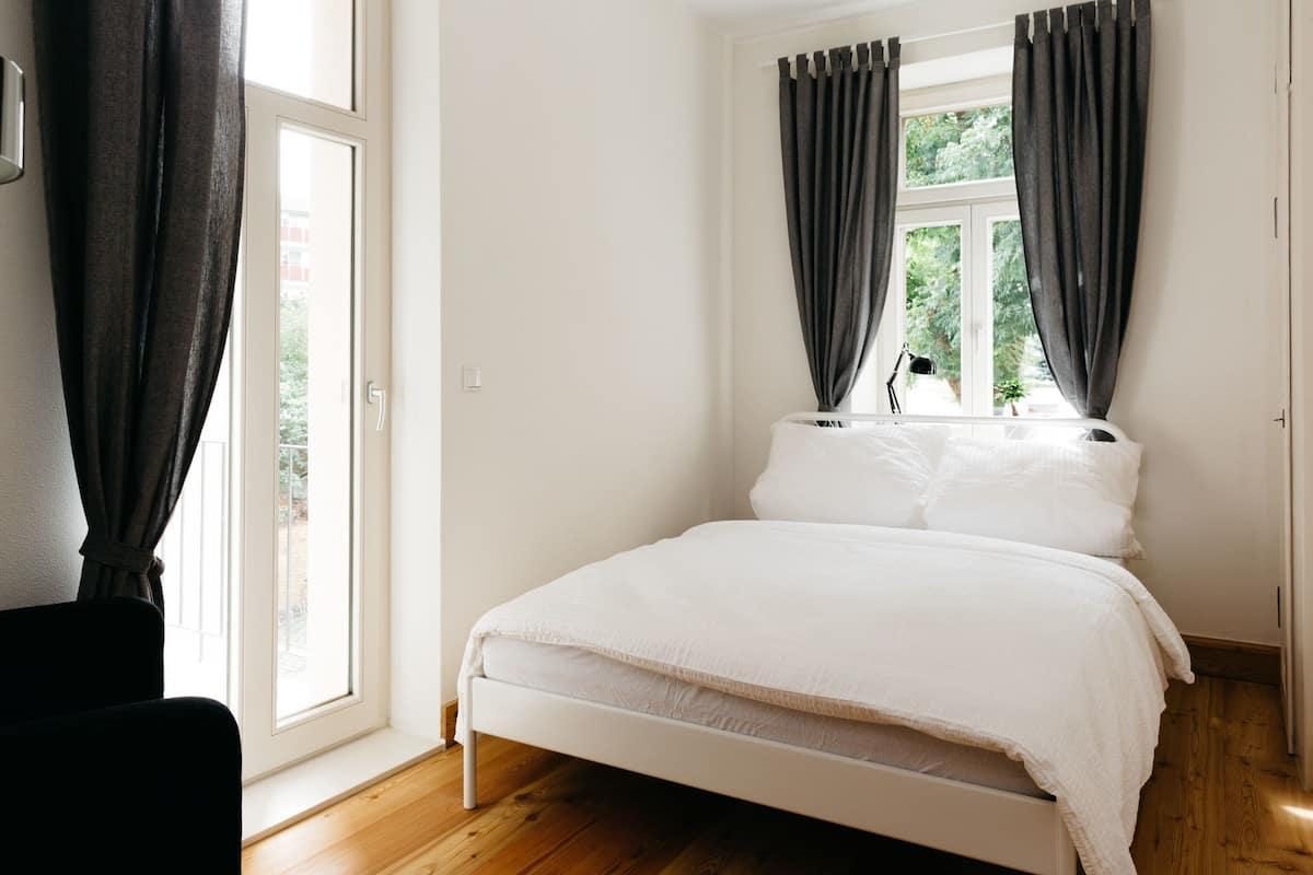 A bedroom with a bed, a window with curtains, and a view of greenery outside.