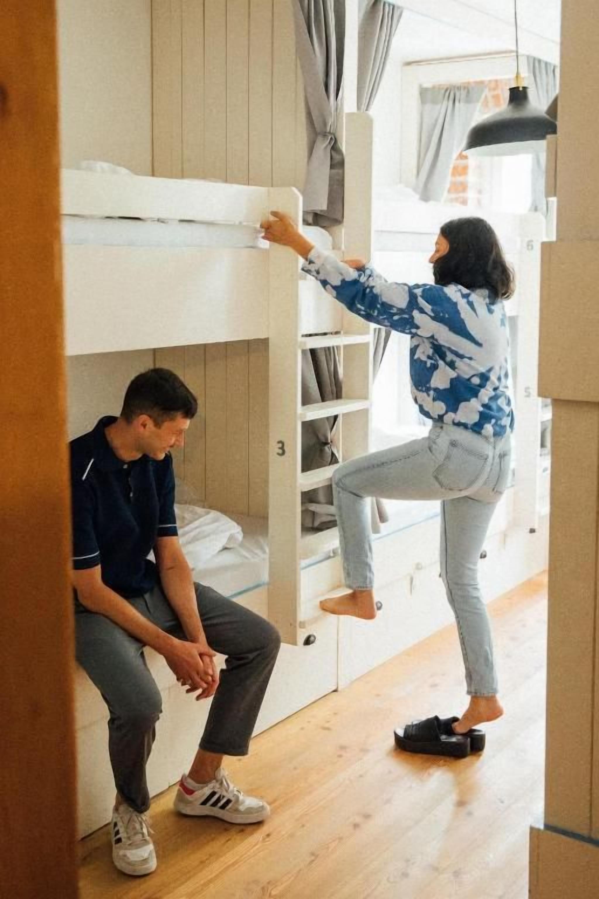 Un letto a castello con una persona seduta sul letto inferiore e un'altra che tende la mano verso il letto superiore.
