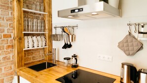 A modern kitchen with a wooden countertop, a black induction cooktop, a stainless steel kettle, and a coffee maker.