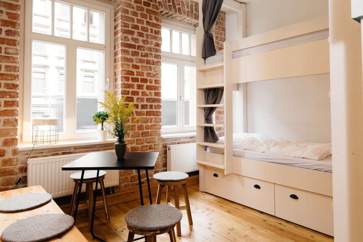 A cozy room with a brick wall, a bunk bed, a dining table with stools, and a potted plant.