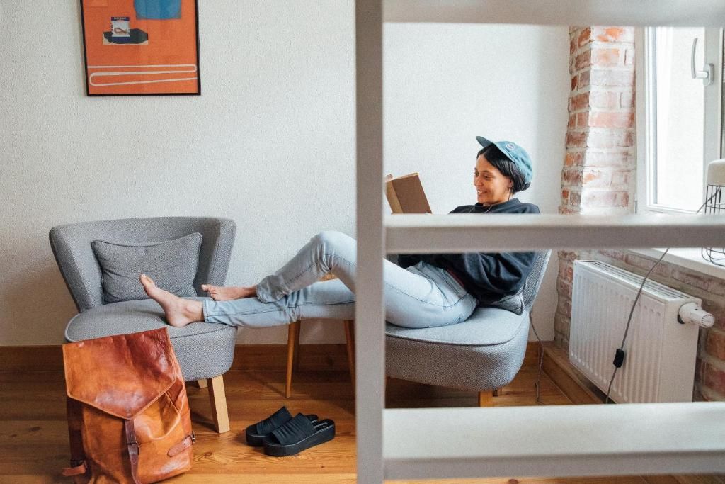Una habitación con un sillón gris, un bolso de cuero marrón y un par de zapatillas negras en el suelo.