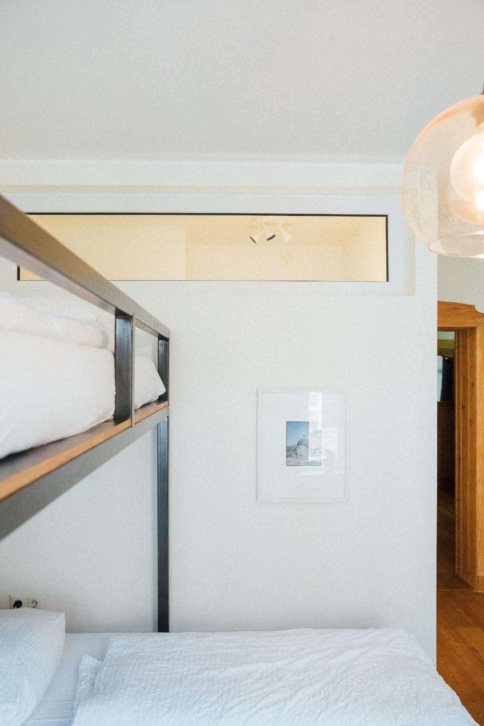 Habitación con literas, cabecero de madera, un cuadro enmarcado en la pared y una lámpara colgante.