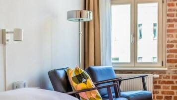 A hotel room with a bed, a chair, a window with curtains, and a lamp.