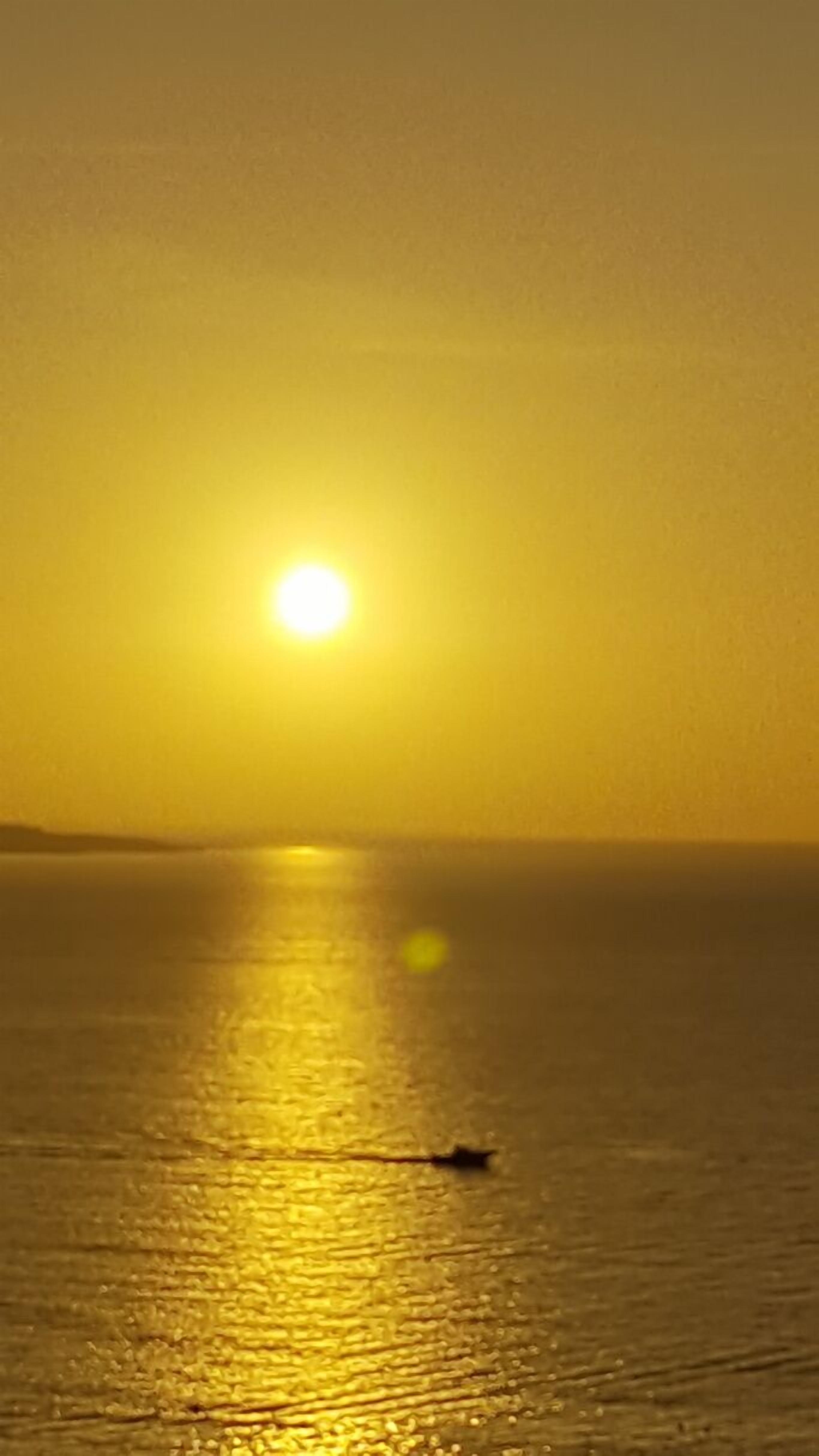 Un coucher de soleil sur une mer calme, avec un bateau à l'horizon.