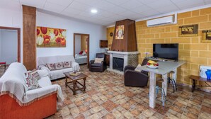 A living room with a fireplace, a sofa, a TV, and a dining area. - Holiday Villa in Seville Countryside. Private pool, a.a., tv sat, free wifi (Lantejuela, La)