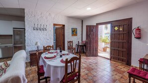A dining area with a white table set for four, wooden chairs, a white textured wall, a door with a metal handle, and a fire extinguisher mounted on the wall. - Holiday Villa in Seville Countryside. Private pool, a.a., tv sat, free wifi (Lantejuela, La)