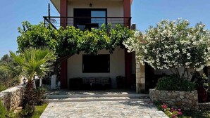 Un edificio a due piani con un vialetto in pietra che conduce all'ingresso, immerso nel verde e circondato da piante fiorite.