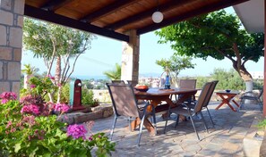 Une terrasse extérieure avec une table et des chaises en pierre, entourée de plantes et d’arbres en fleurs.