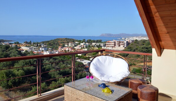 Un balcon avec une table en osier, un coussin blanc et deux verres.