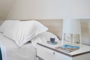 A neatly made bed with white linens, a bedside table with a lamp, a cup, and a magazine. - Sea View Central in Amalfi 2BR (Amalfi)