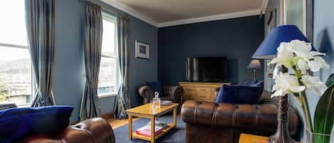A living room with leather sofas, a coffee table, a TV, and a window with curtains.
