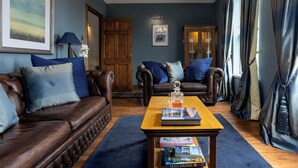 Un salon avec un canapé en cuir marron, une table basse en bois sur laquelle sont posés des livres et un tapis bleu.