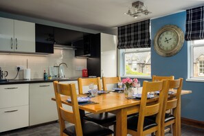 A modern kitchen with white cabinets, a dining table set for four, and a large wall clock. - 2BDR Historic Home in Heart of Edinburgh (Edinburgh)