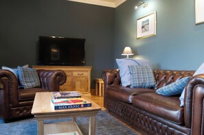 A living room with two leather sofas, a coffee table with books, a television, and a lamp.