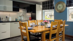Une cuisine moderne avec des meubles blancs, une table à manger dressée pour quatre personnes et une grande horloge murale.