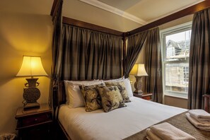 A hotel room with a large bed, two bedside lamps, a window with curtains, and a view of the outside.