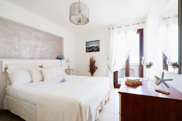 A bedroom with a large bed, a wooden dresser, a small table, a starfish decoration, and a painting on the wall.