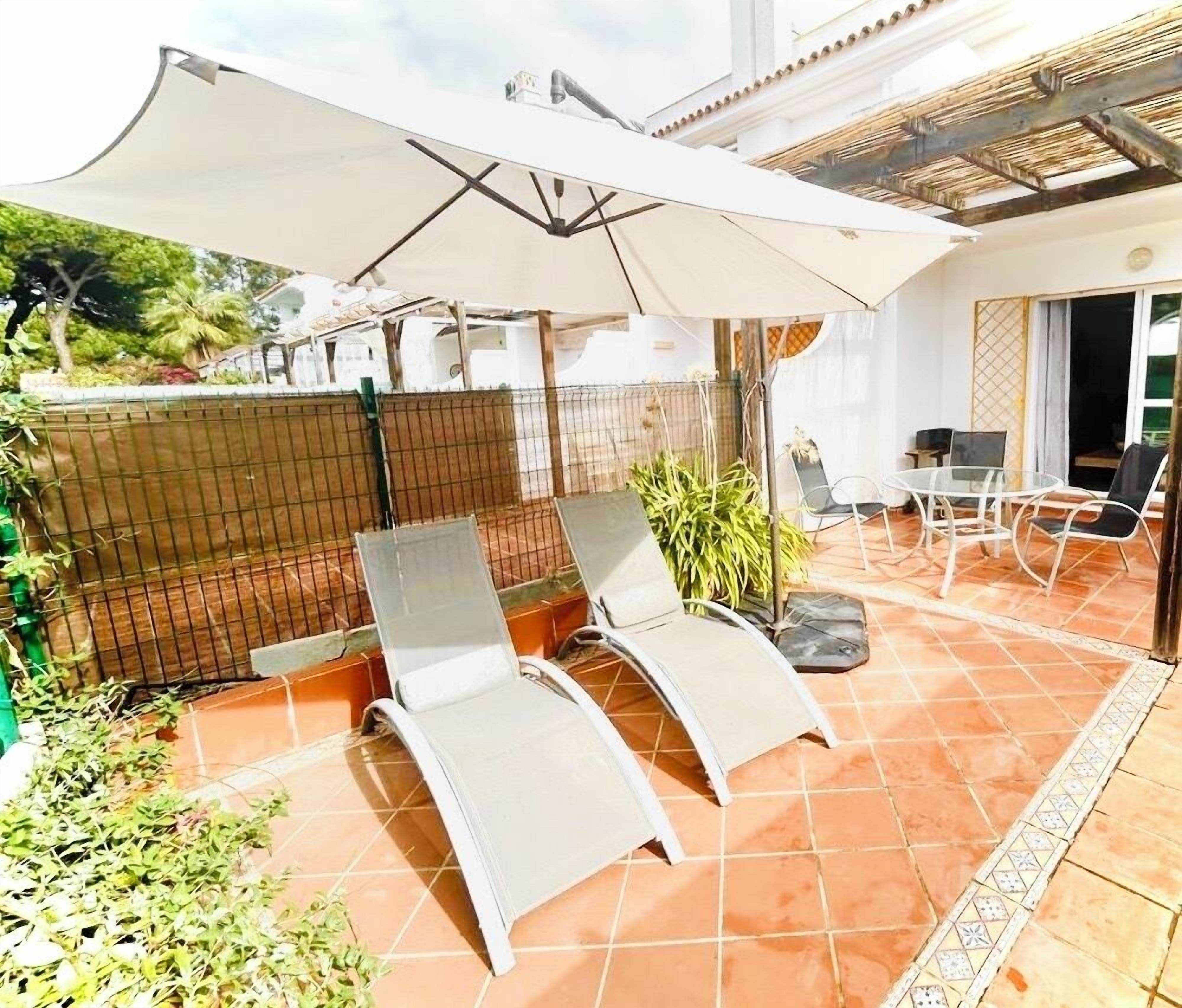 A patio with two lounge chairs, a table, and a large umbrella.