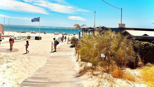 A beach with a wooden boardwalk leading to the water, umbrellas, and beachgoers. - Splendid, luxurious beach holiday house near fishing villages. A/C pool** (Nuevo Portil)