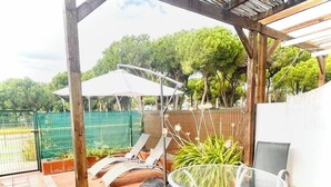 A covered patio with a table and chairs, a potted plant, and a tennis court in the background. - Splendid, luxurious beach holiday house near fishing villages. A/C pool** (Nuevo Portil)