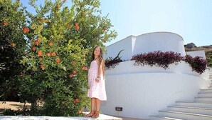 Une personne se tient sur une corniche en pierre, avec un bâtiment blanc et des marches en arrière-plan.