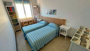 Ein Schlafzimmer mit zwei Betten, einem Schreibtisch, einem Stuhl, einem Bücherregal und einem Nachttisch.