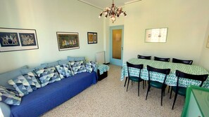 A room with a blue sofa, a dining table with chairs, and framed pictures on the walls.