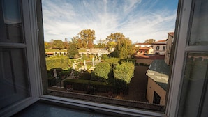 Blick aus einem Fenster auf einen Garten mit Statuen und einem Gebäude im Hintergrund.