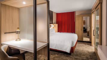 A hotel room with a bed, a desk, a chair, a lamp, and a mirror.