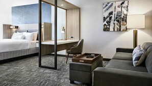 A hotel room with a bed, a desk, a sofa, and a large abstract painting on the wall.