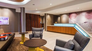 A modern reception area with a wooden reception desk, grey upholstered seating, and a round table with a yellow base.