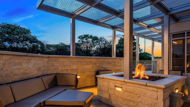 An outdoor patio with a stone fire pit and seating area, enclosed by a glass roof.