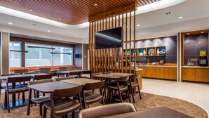 A modern restaurant interior with wooden tables and chairs, a large TV screen, and a counter with a coffee machine.